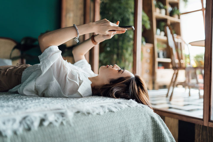 Woman Looking At Phone Upside Down In Bed